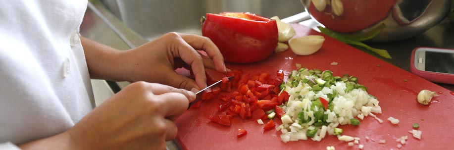 Student preparing chopping peppers in the hospitality kitchen.