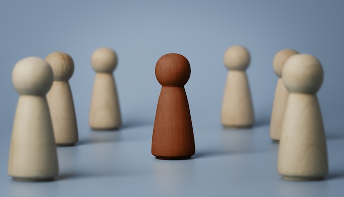 One Red Chess Piece in Middle of Group of Surrounding White Chess Pieces