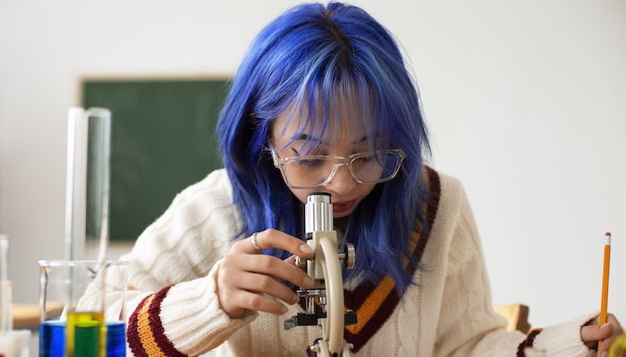 Biology Student Looking Through Microscope and Taking Notes