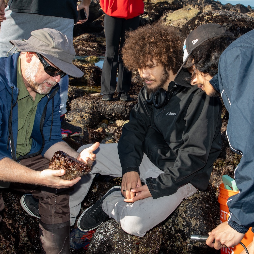 environmental science teacher showing students rock at ocean field trip