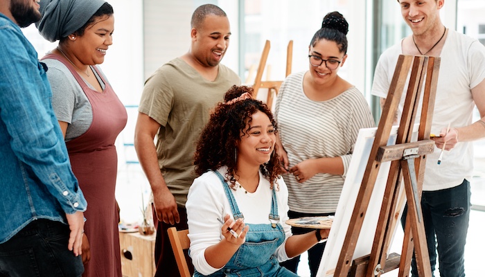 Standing Artists Gathering Around One Sitting Artist Looking at Her Easel