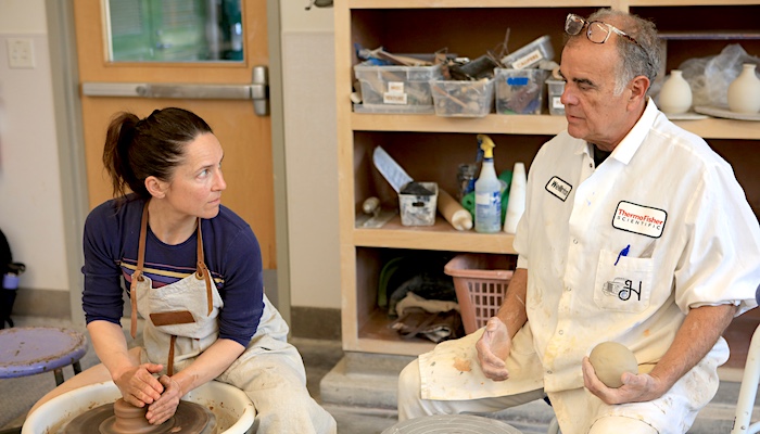 Ceramic Student Throwing on the Wheel Listening to Instructor in Class