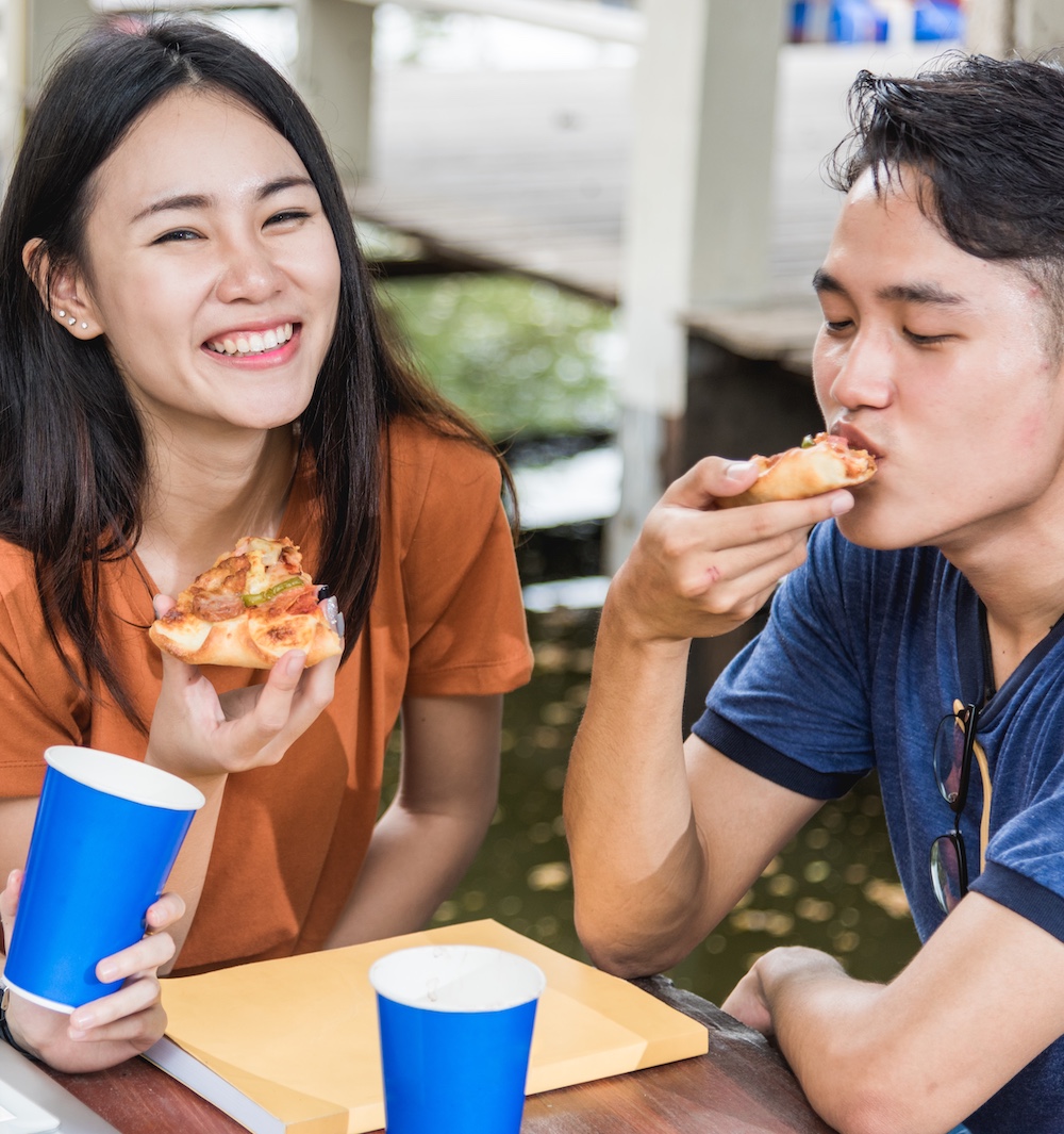 Two People Smiling and Eating Pizza