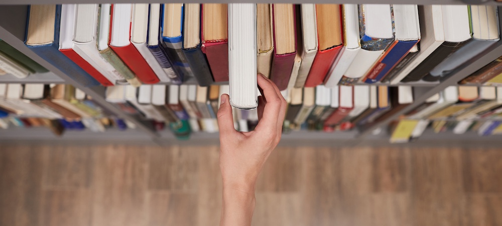 Person Grabbing Book off Bookshelf