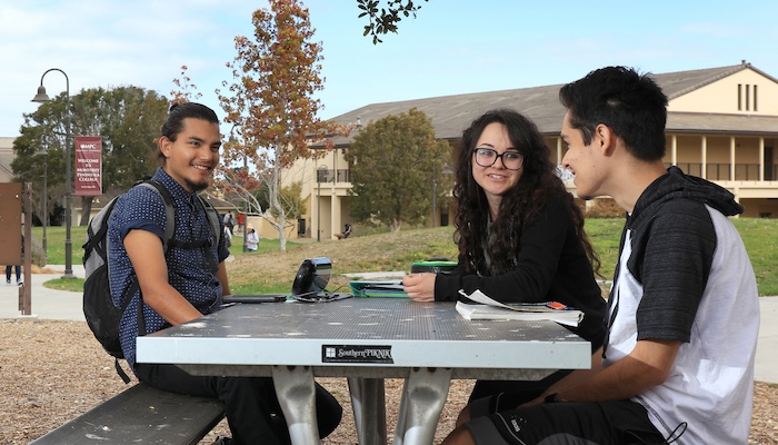 Three Students Sitting Outside at Picnic Table